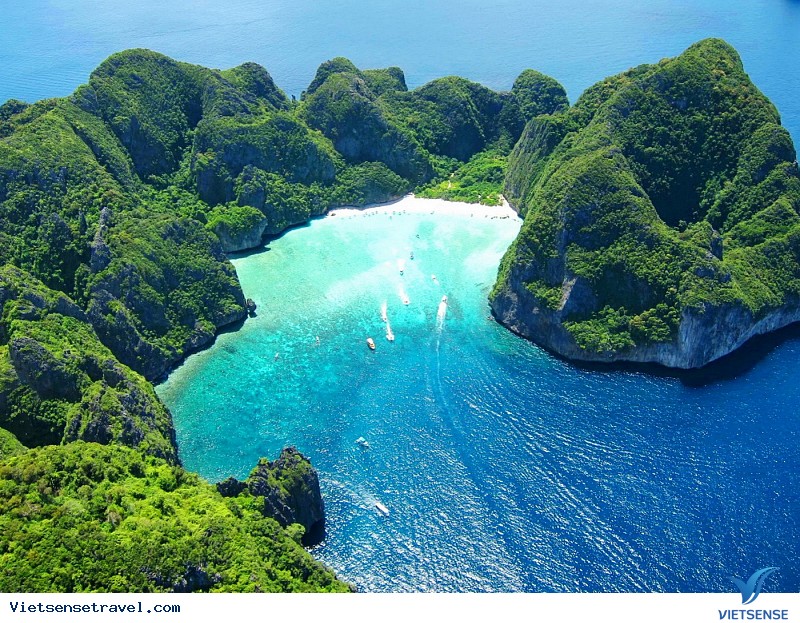 Thuyền longtail trên bãi biển cát trắng với hàng dừa và núi đá vôi